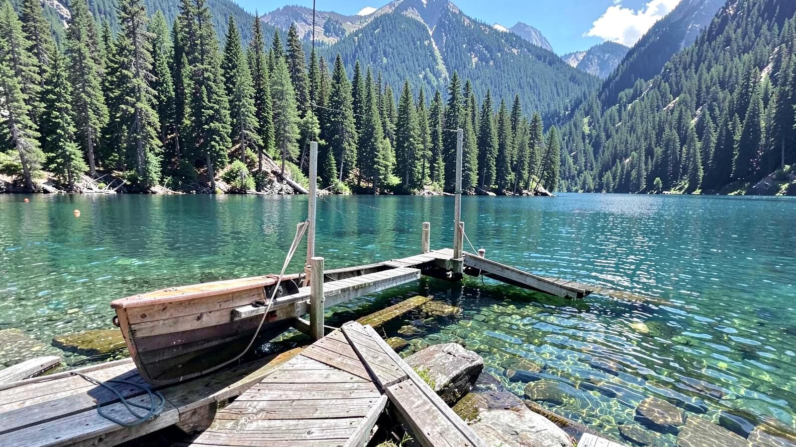Wooden dock and boat lift posts on a clear forested mountain lake in summer