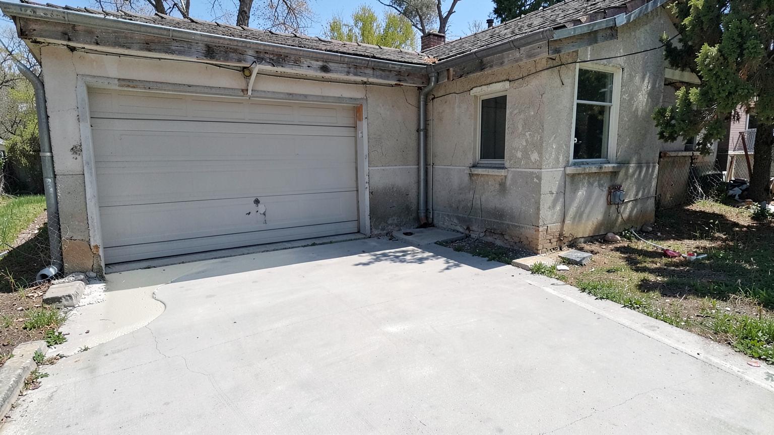 Freshly poured smooth concrete driveway beside a modest older house with a plain white garage door