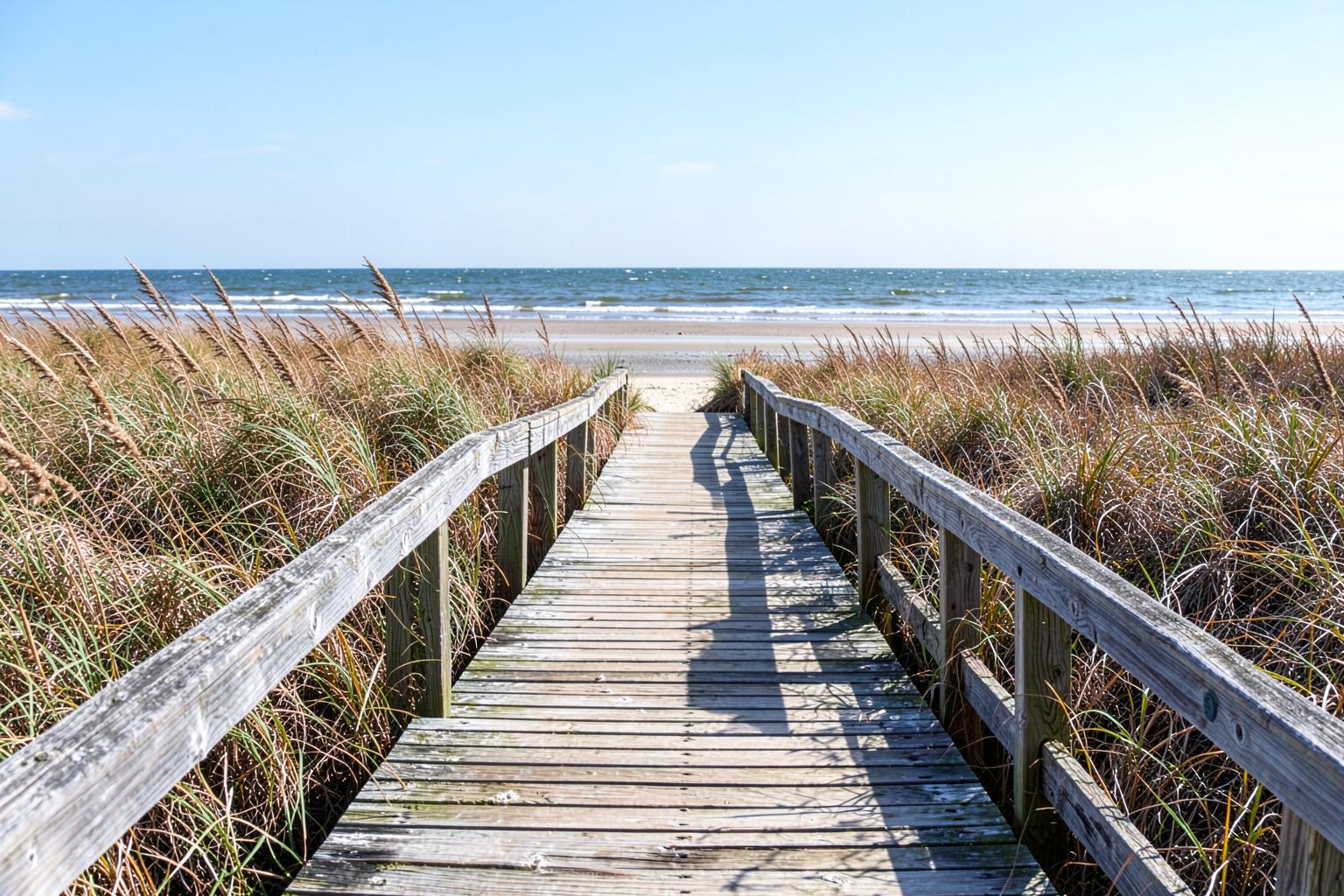 Weathered wooden walkway crossing dunes and sea oats toward a wide Atlantic beach