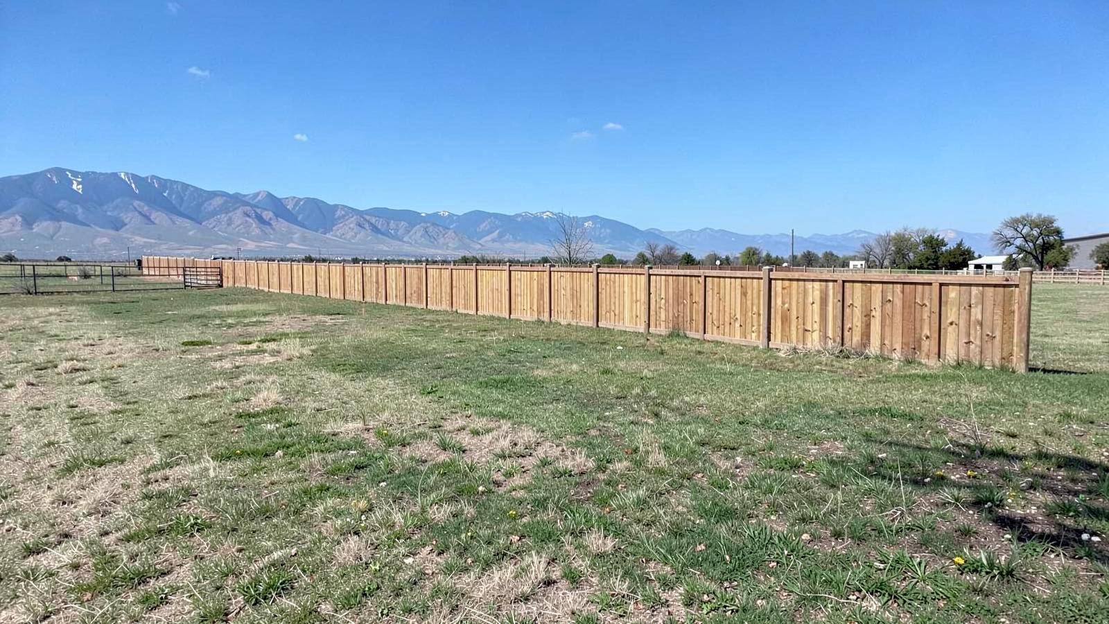 Long new cedar fence running along the edge of open flat farmland under a wide blue sky