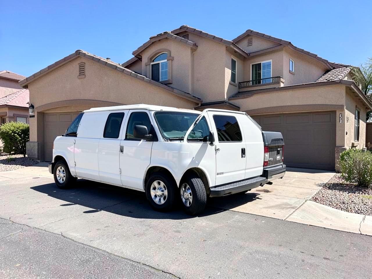 Plain white service van parked in the driveway of a newer stucco suburban home at midday
