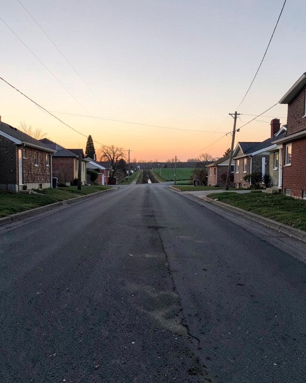 Empty residential street at sunrise with an irrigation ditch and farm field at the end of the block