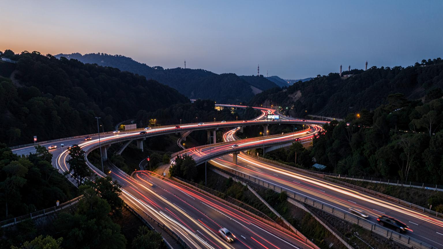 Stacked interstate interchange curving above tree-lined suburbs at dusk with headlights streaking across the lanes