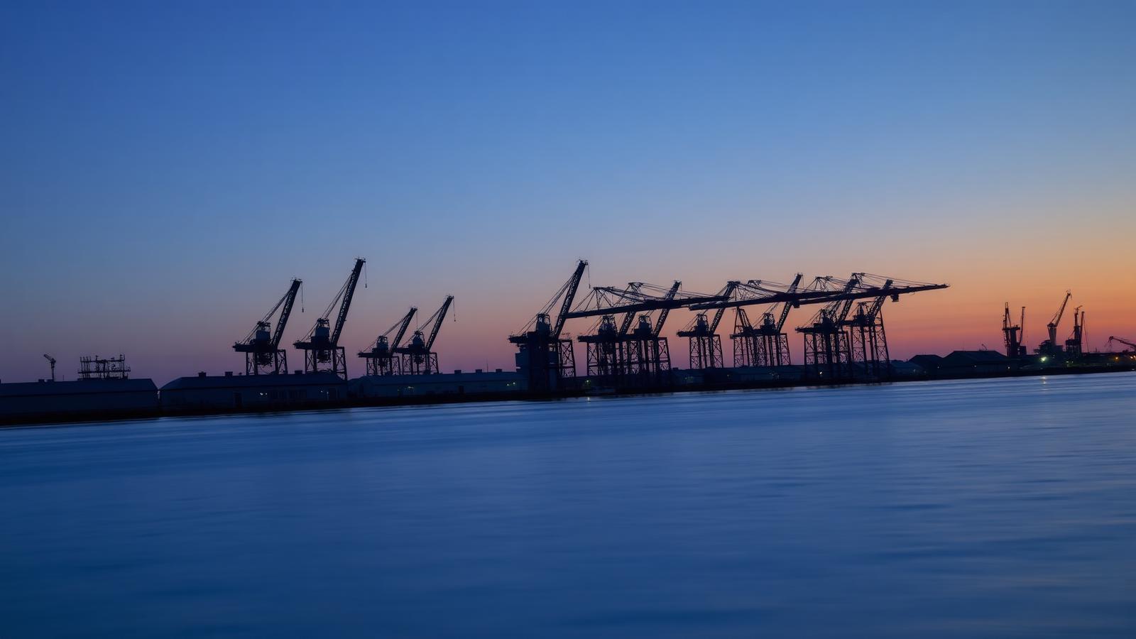 Dock cranes silhouetted along the Erie harbor at dusk over calm freshwater