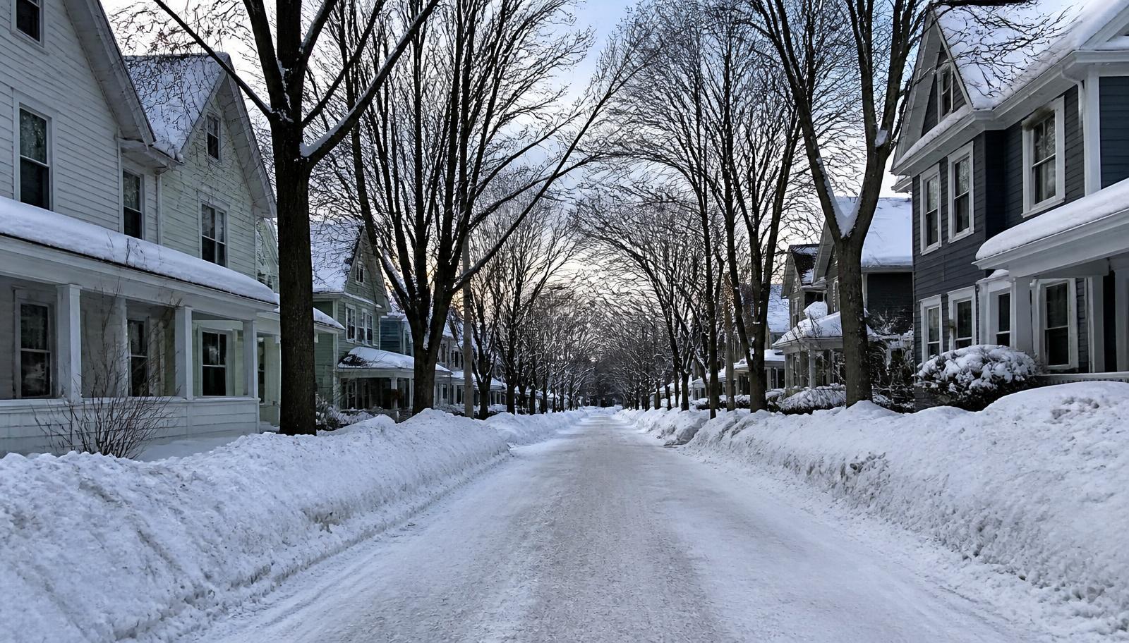 Older wood-sided homes along a snow-covered Erie residential street with tall plowed snowbanks