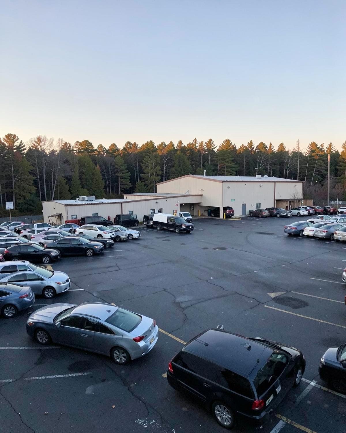 Full employee parking lot outside a low industrial building at shift change in the inland Upstate at dawn
