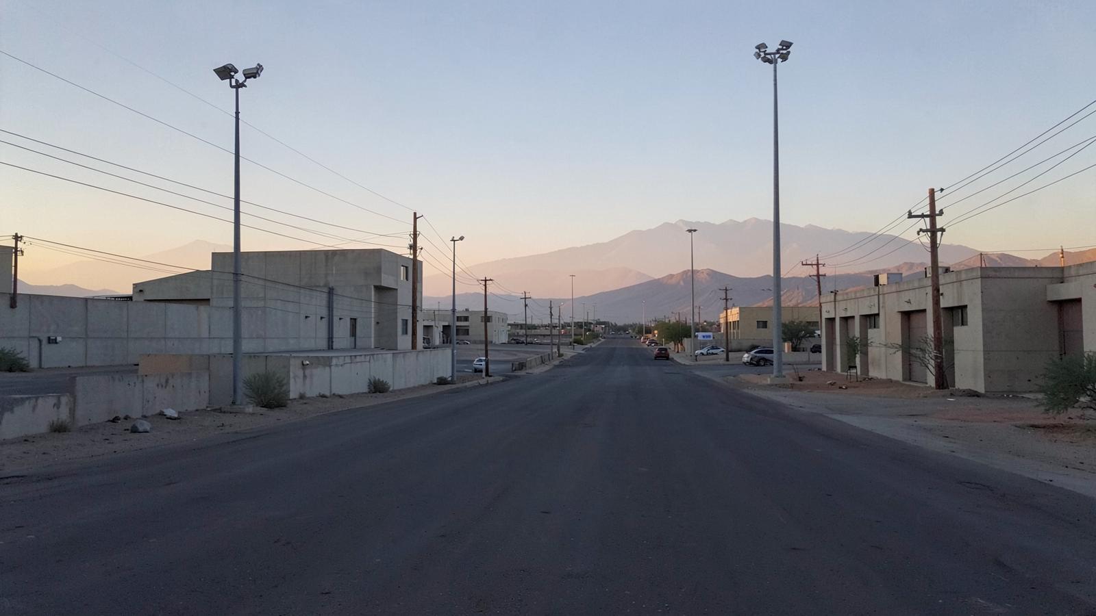 Empty wide boulevard in a desert industrial district at dawn with blank concrete buildings and distant mountains
