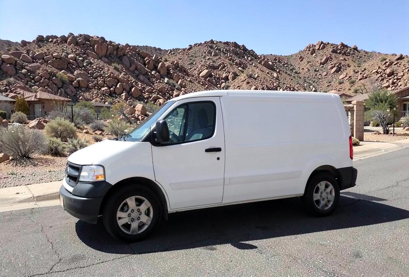 Plain unmarked white service van parked on a quiet desert residential street with rocky hills behind