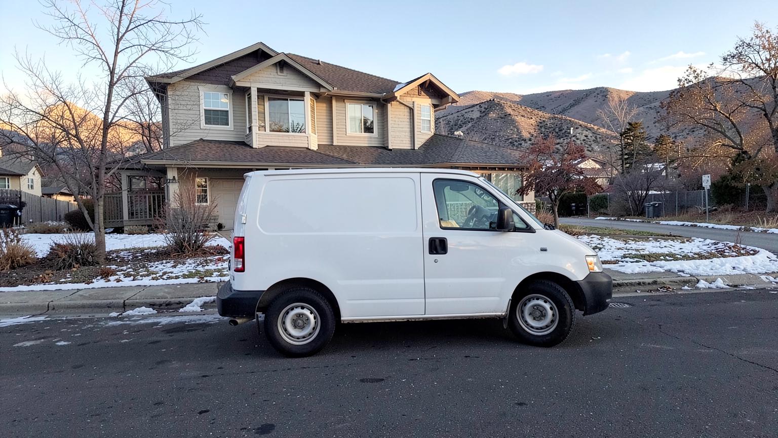 Plain white work van parked on a residential street with bare winter trees and foothills in the distance
