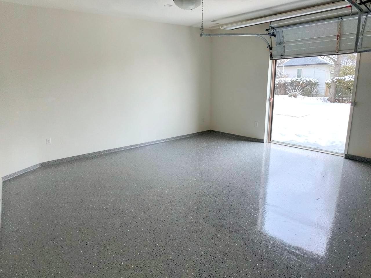 Freshly coated glossy grey epoxy garage floor in an empty two car garage with the door open to daylight