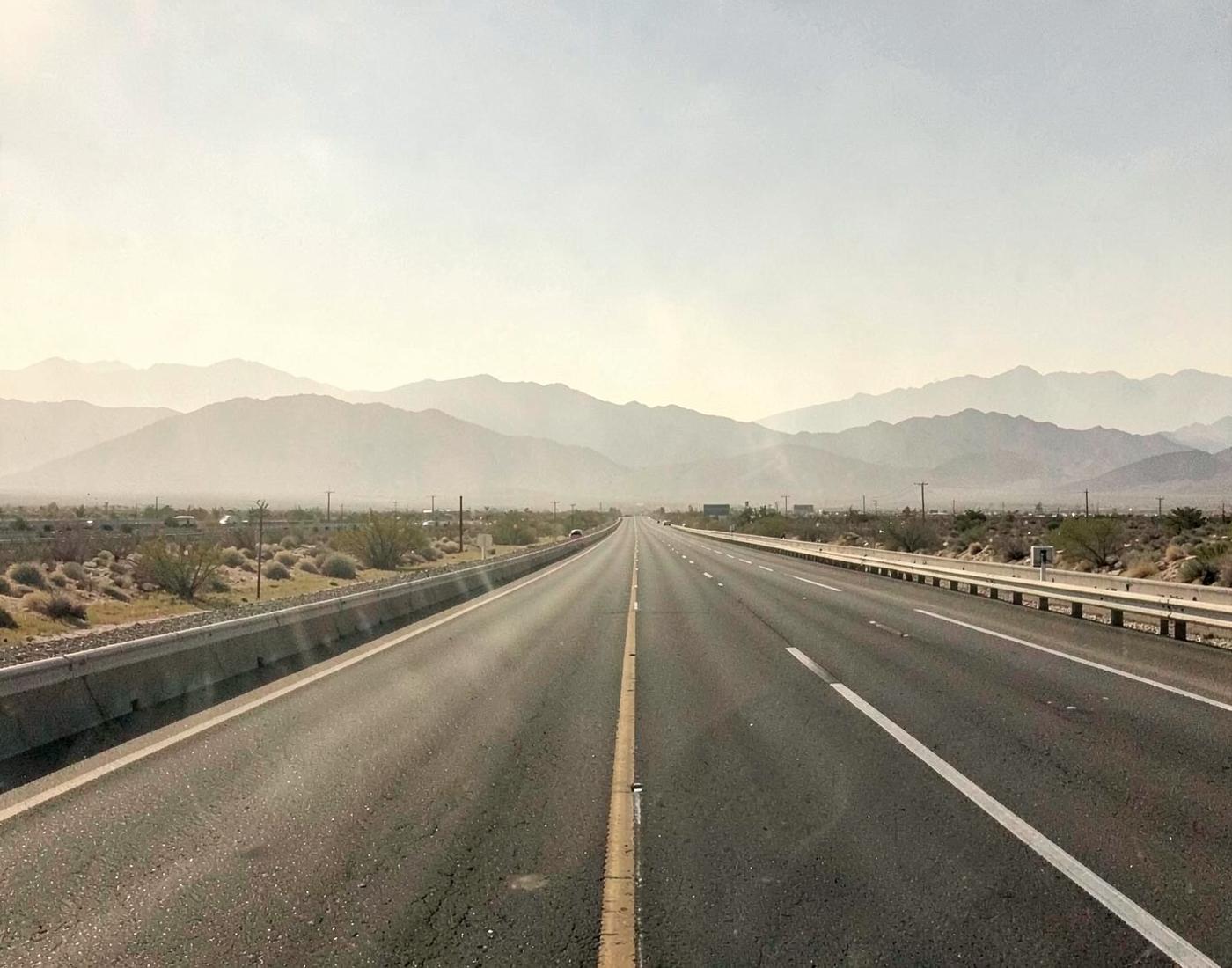 Heat shimmer rising off an empty multi-lane desert freeway with mountains blurred in haze