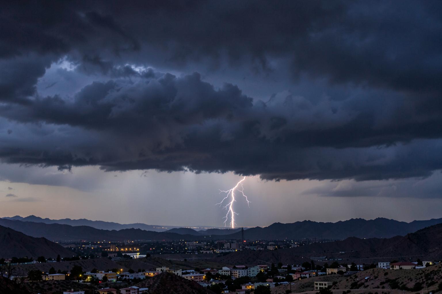 Monsoon thunderstorm clouds and distant lightning building over a desert valley city at dusk