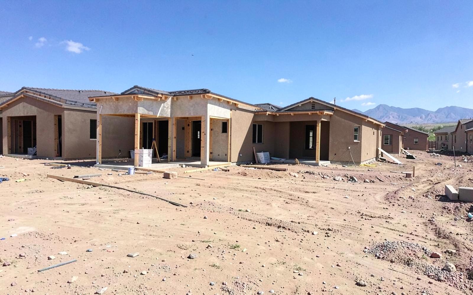 New home construction with framing and stucco in a large desert subdivision under a bright blue sky