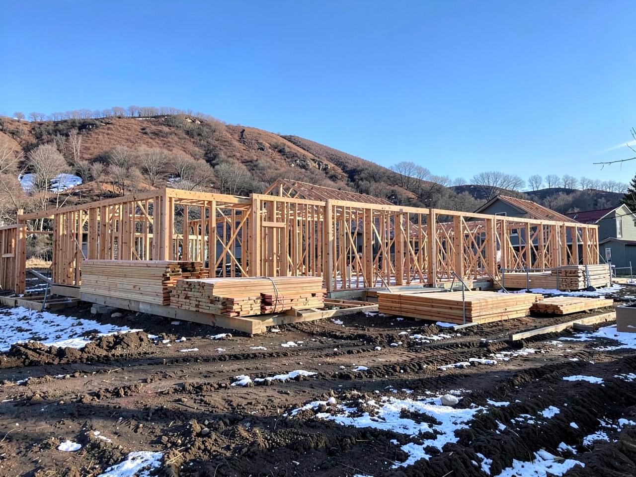 Wood framed houses under construction in a new subdivision with graded dirt lots and mountains behind