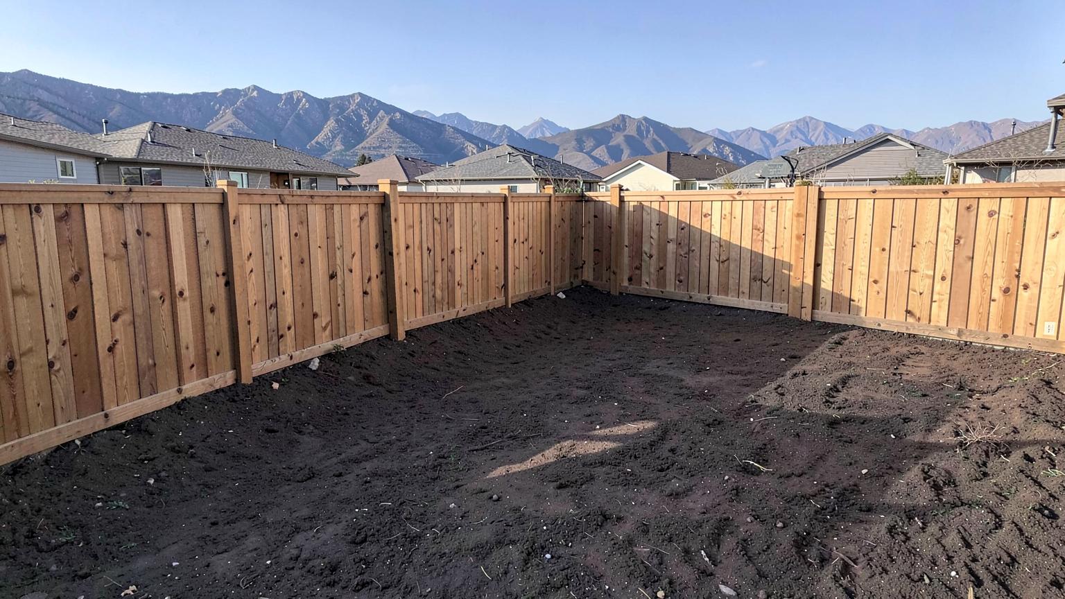 Newly installed vinyl privacy fence enclosing a bare dirt backyard behind a recently built two story home