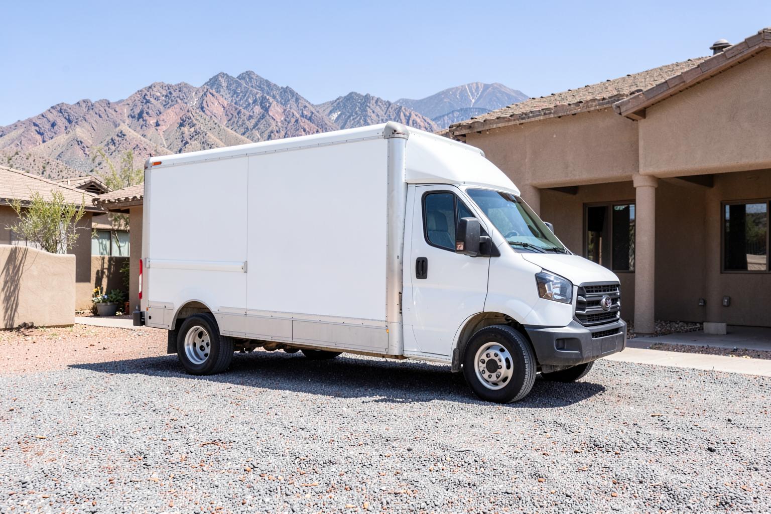 Plain unmarked white cargo van parked in a gravel driveway of a desert home under bright sun