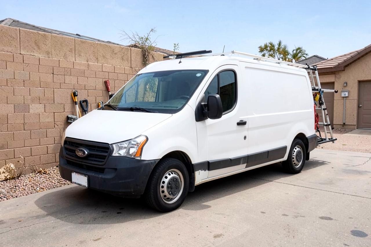 Plain unmarked white service van with a ladder rack parked in a suburban desert driveway beside a block wall