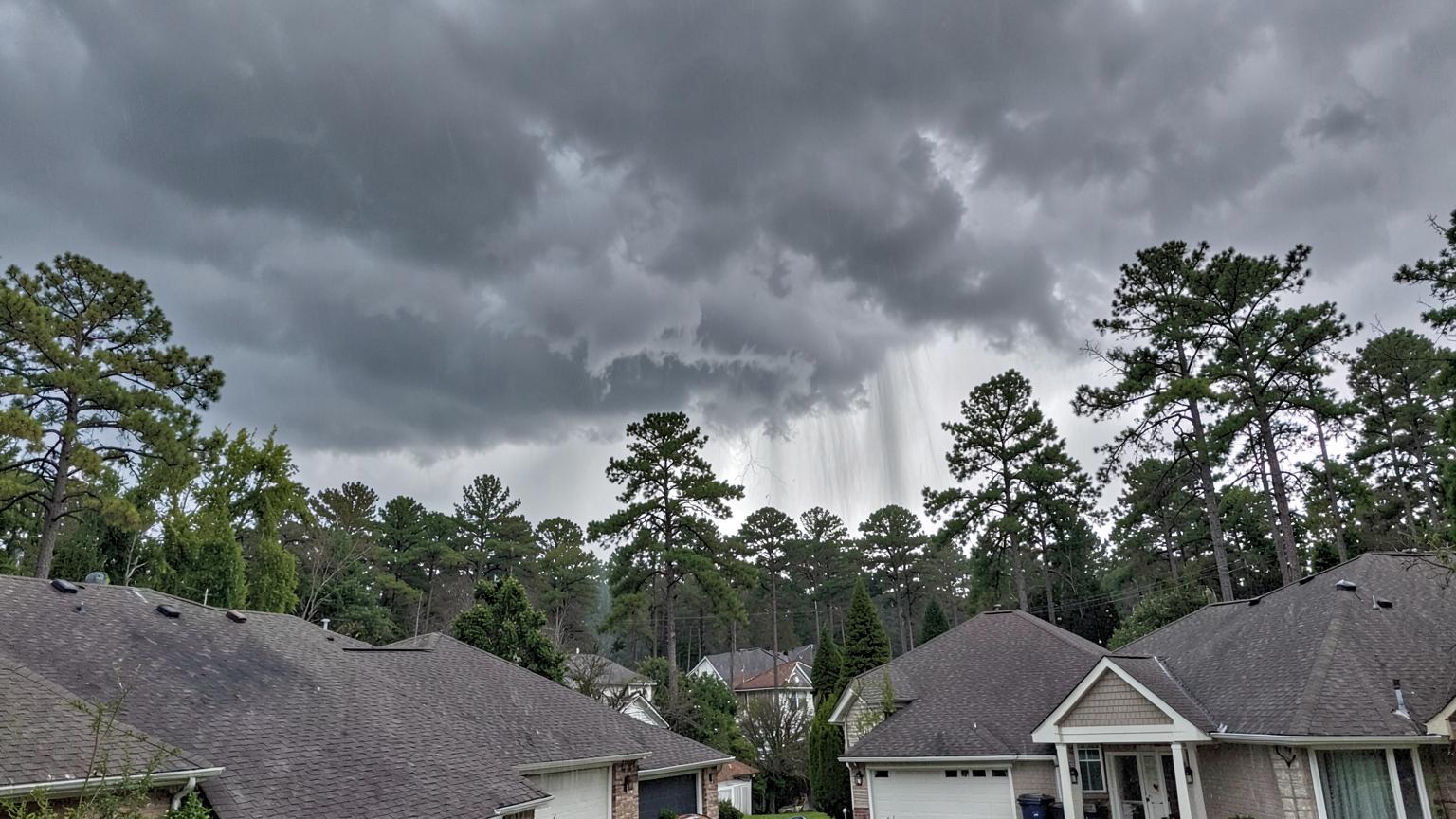 Dark thunderstorm clouds building over the rooftops of a wooded suburban neighbourhood