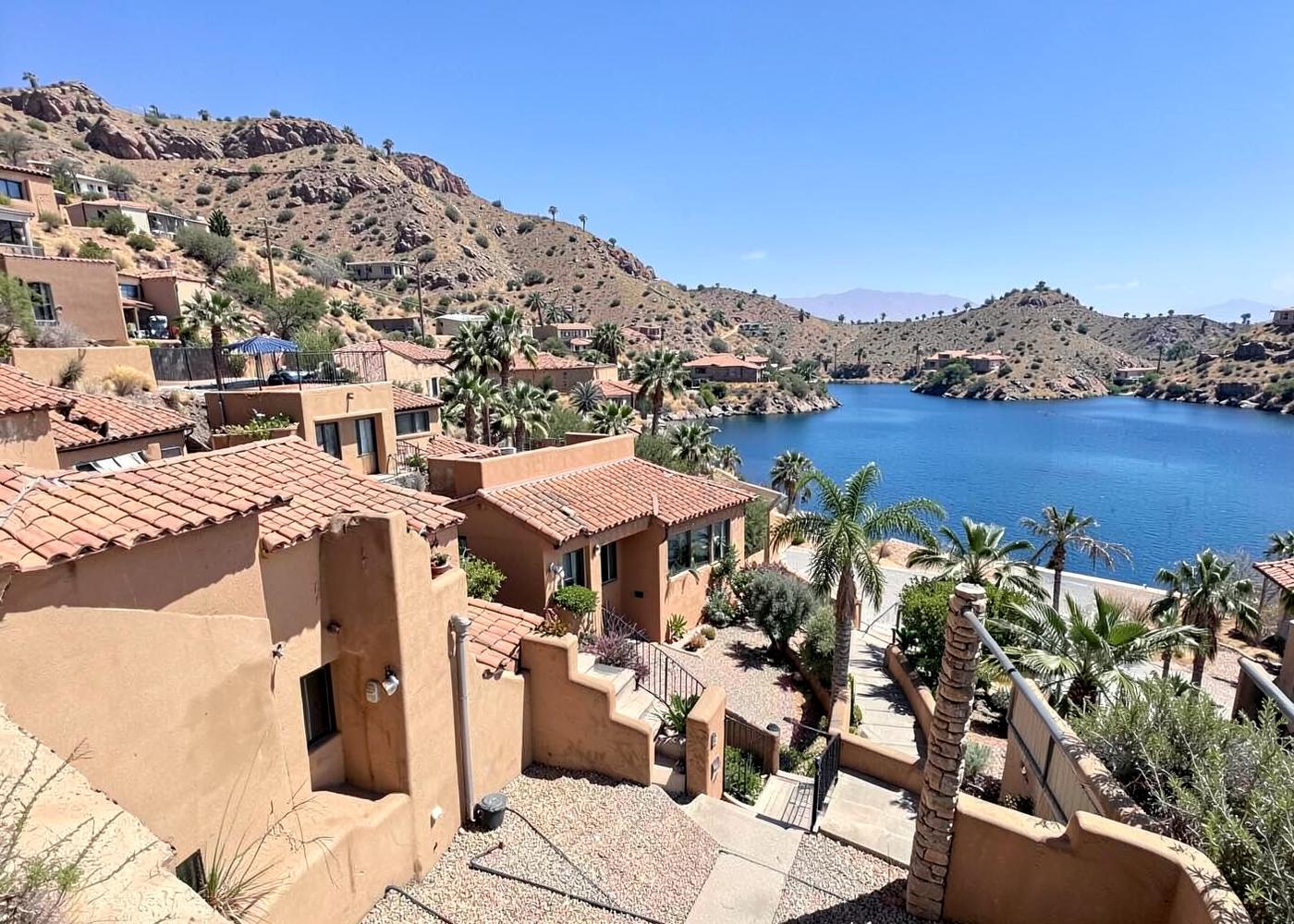 Sunlit hillside neighbourhood of stucco homes with tile roofs and palms stepping down toward a blue desert lake