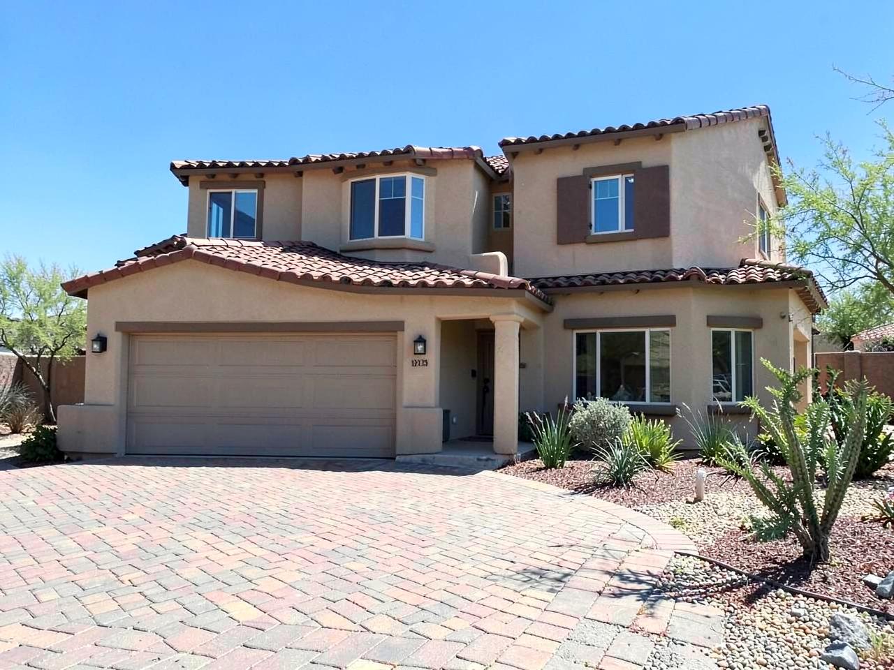 Newly built two-story stucco home with a tile roof and paver driveway under bright desert sun