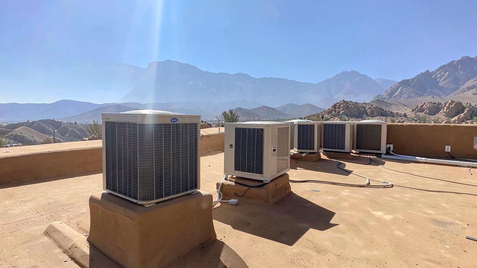 Rows of rooftop air conditioning condenser units on a low building under intense desert sunlight