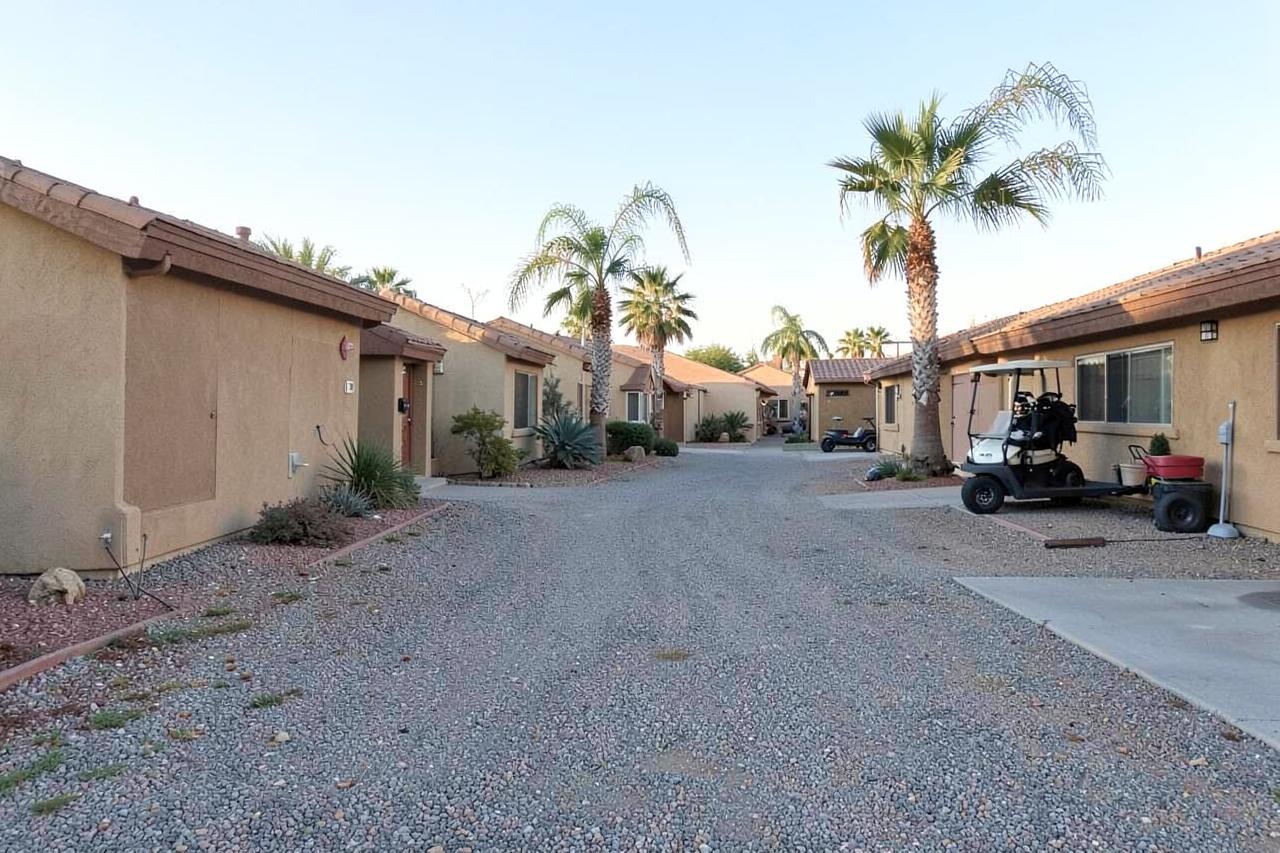 Quiet cul-de-sac of single-storey stucco homes with gravel yards, palms and a golf cart in a desert retirement community