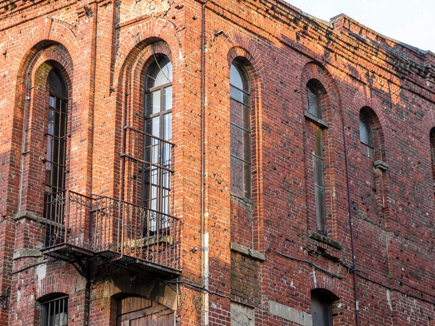 Tall arched windows of a converted red brick riverside mill building with weathered masonry and iron detailing