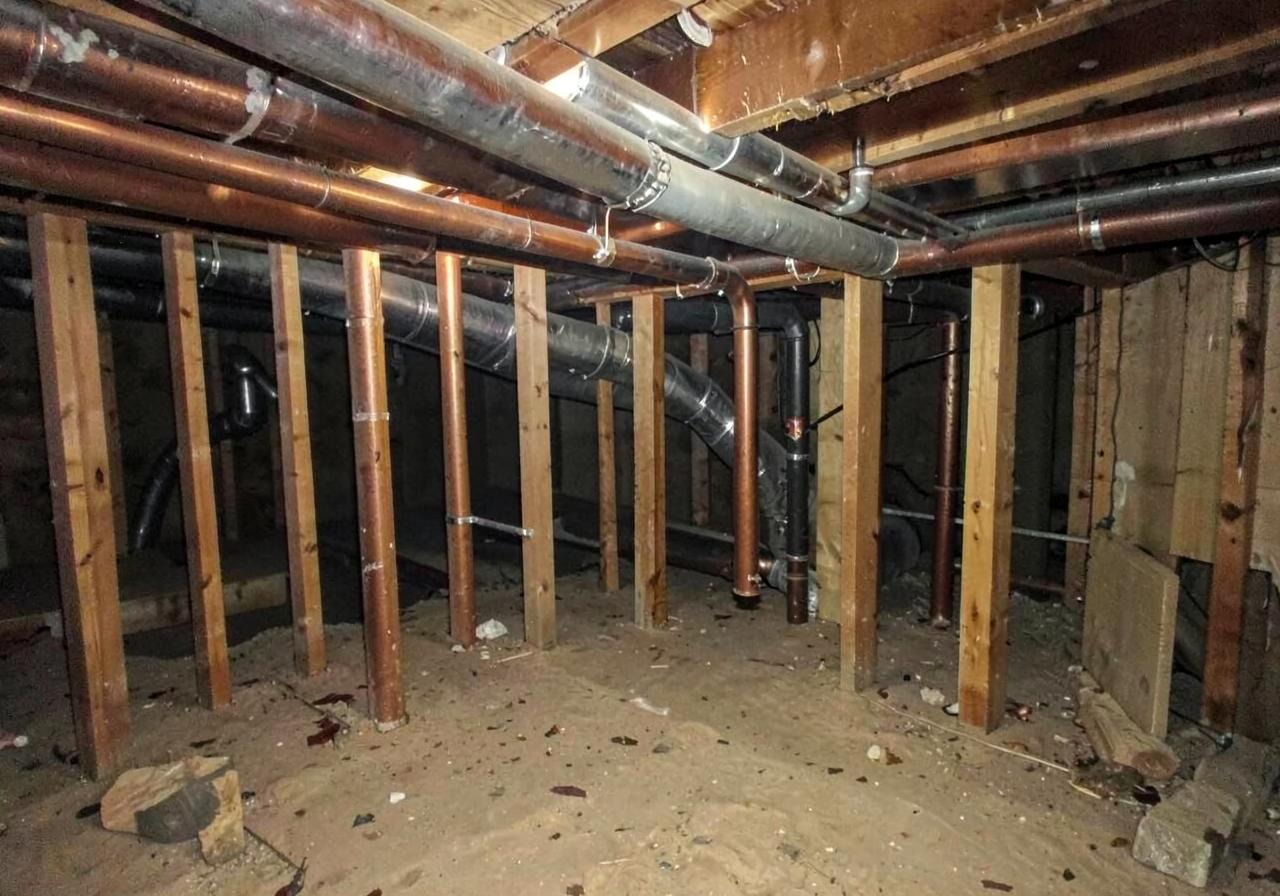 Copper pipes and new insulated ductwork running through open floor joists under a house