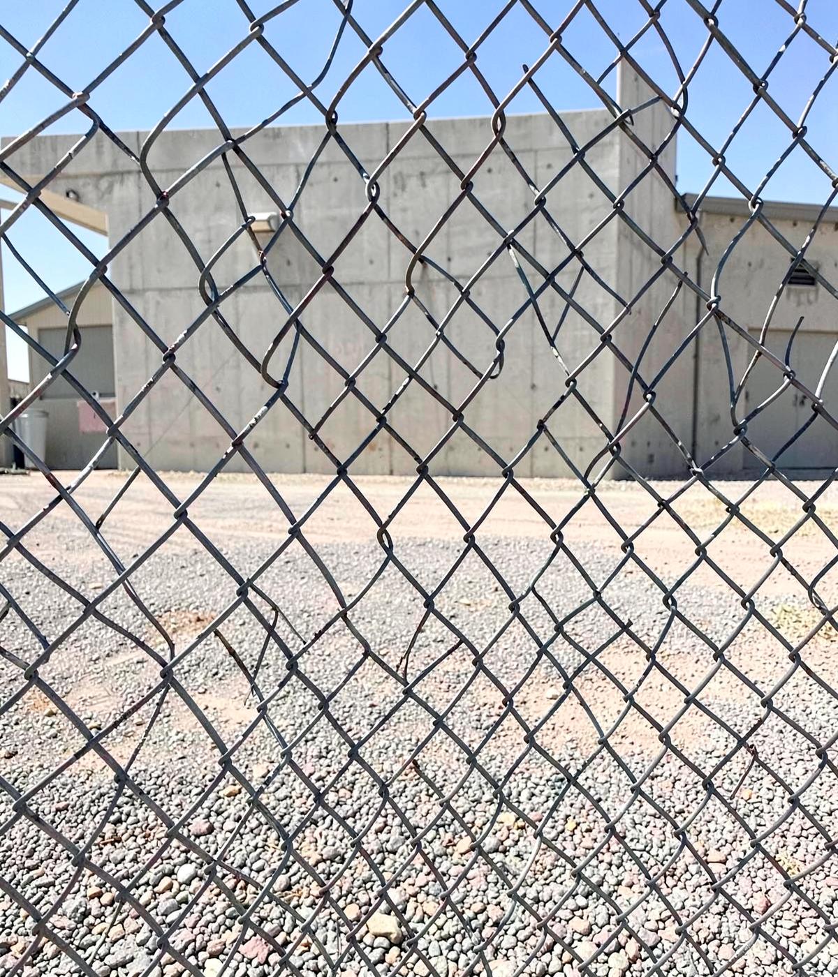 Chain link fence and gravel lot in front of a plain concrete industrial building in bright desert light