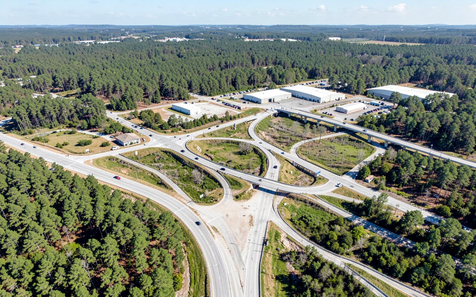 Aerial view of a highway interchange surrounded by pine forest and light industrial warehouses in the inland South