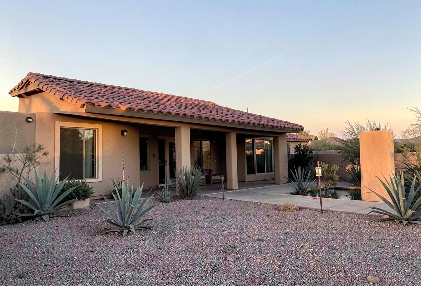 Desert lakeside home with a tile roof, covered patio, agave and gravel yard in warm evening light