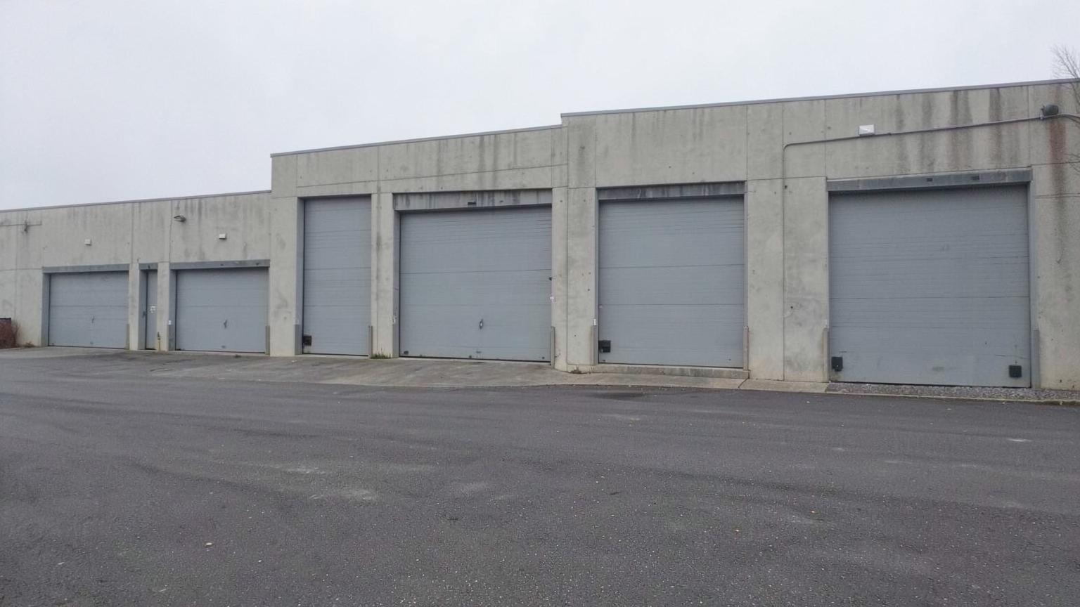 Row of closed grey loading dock doors along a blank concrete warehouse wall beside an empty asphalt yard