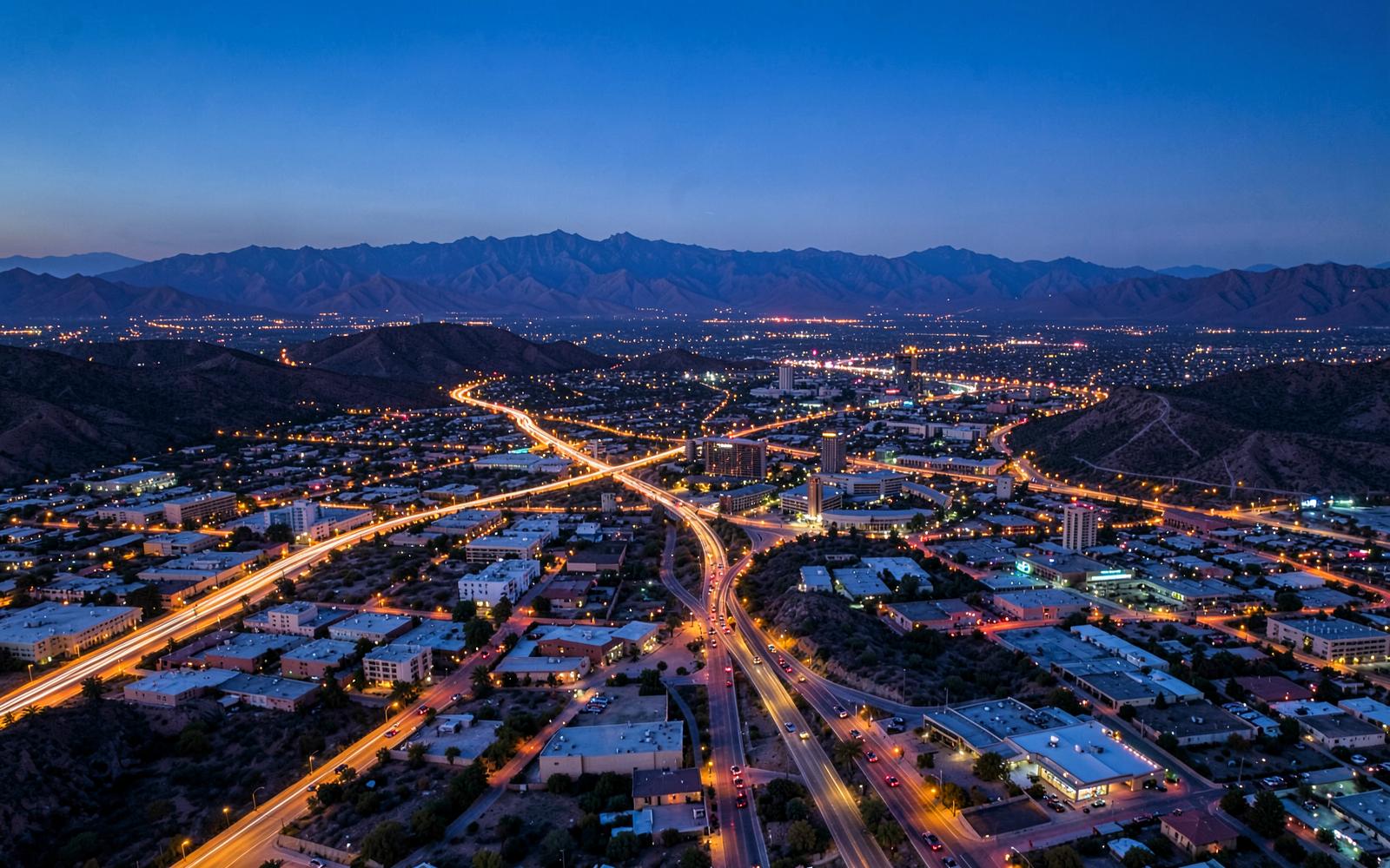 Sprawling desert metropolis at dusk seen from the air with freeway lights threading between mountain ranges