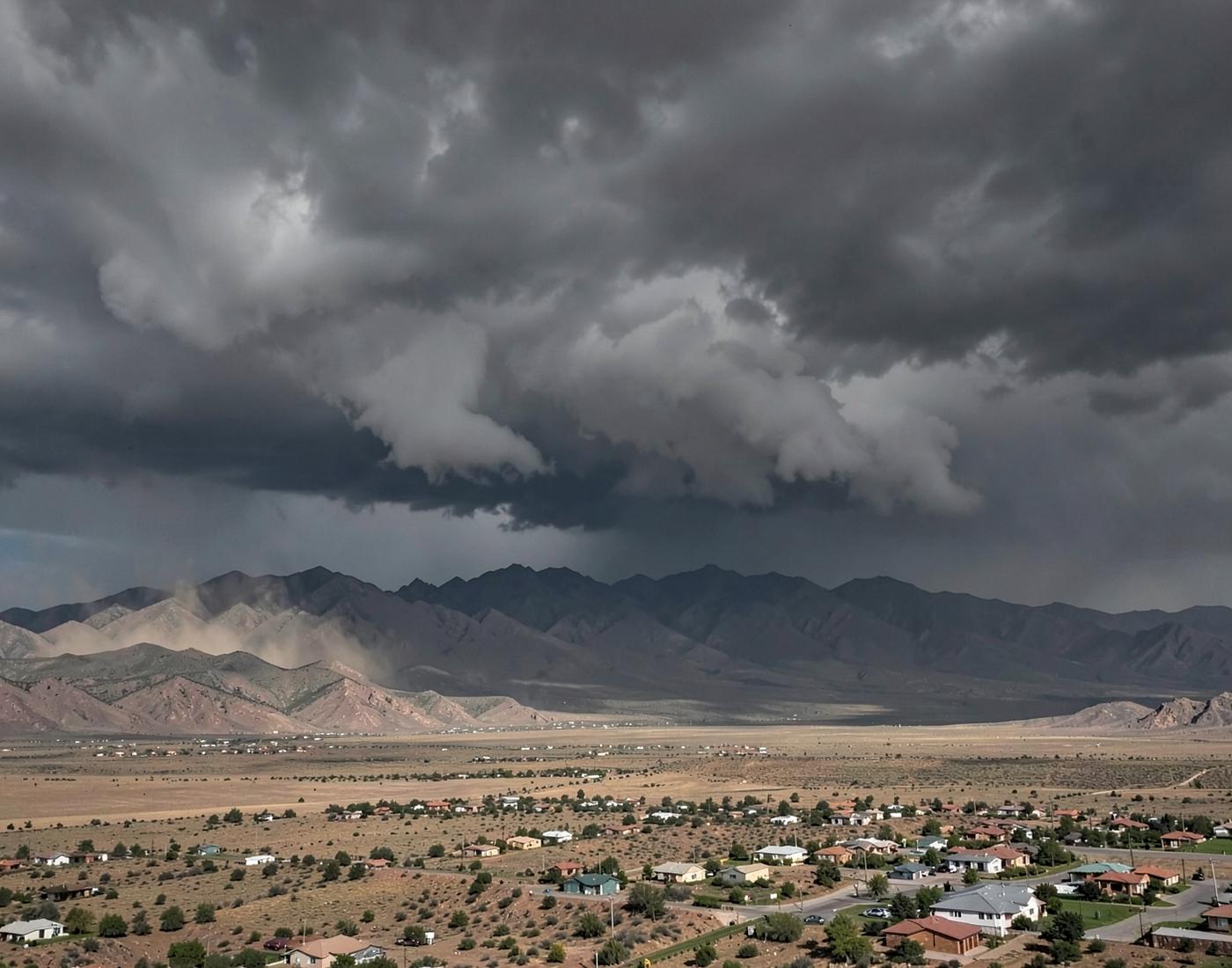 Monsoon storm clouds and blowing dust building over desert mountains above a wide valley of houses
