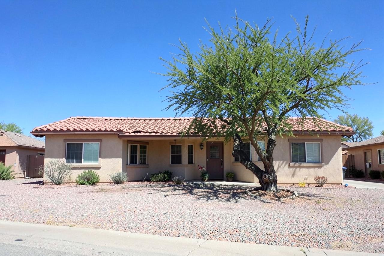 Single-storey stucco ranch home with tile roof, gravel yard and a mature palo verde tree under clear blue sky