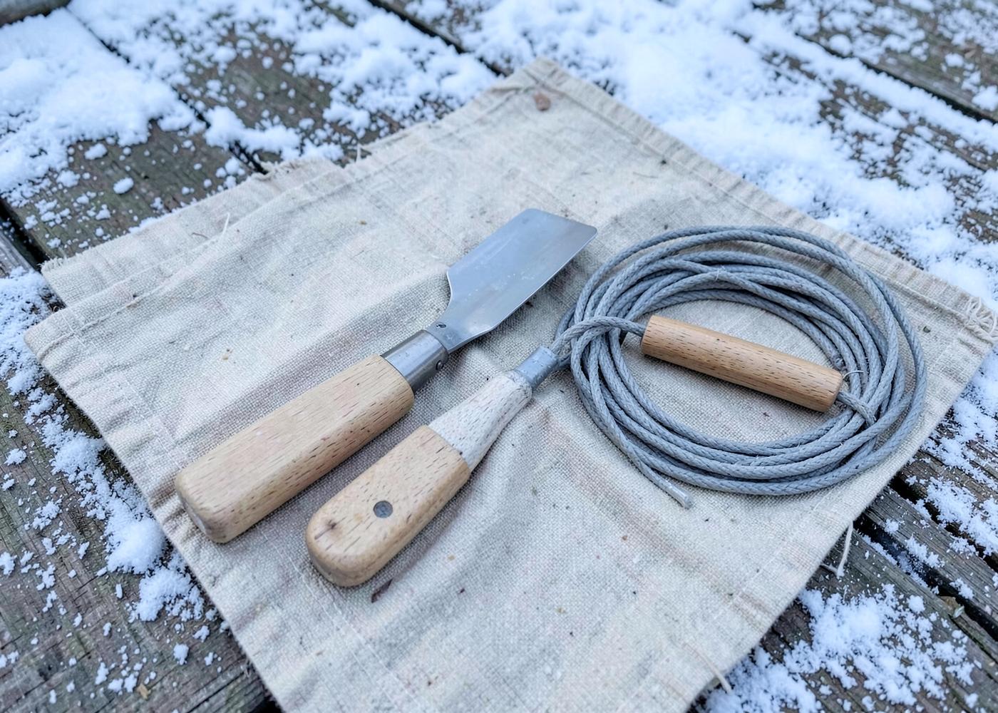 Plain hand tools and a coil of grey wire laid out on a canvas tarp on snow-dusted deck boards