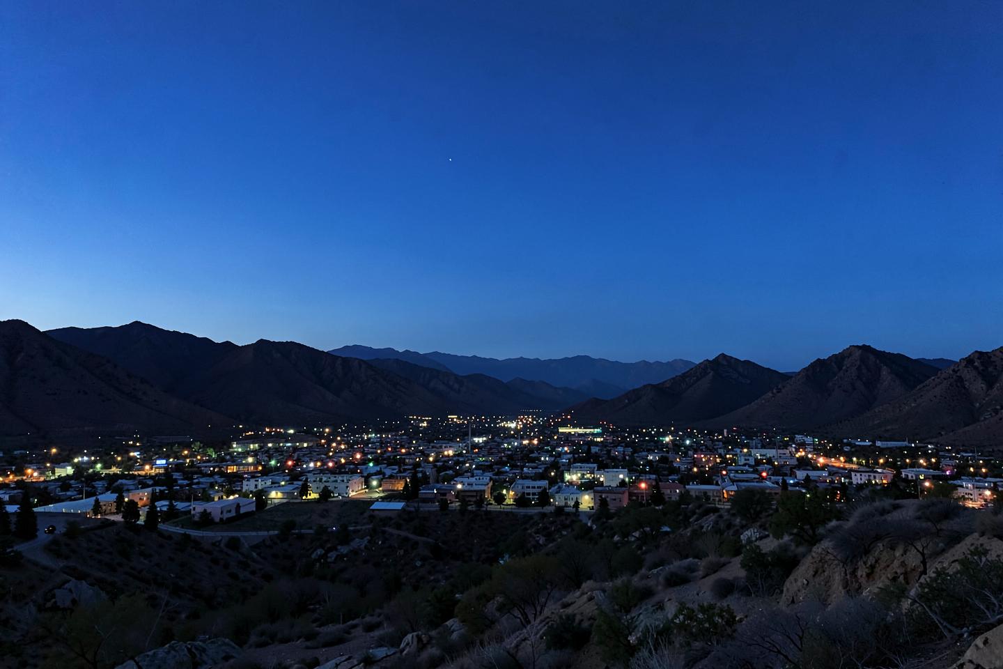 High-desert valley city lights at dusk beneath dark mountain ridges and a deep blue sky