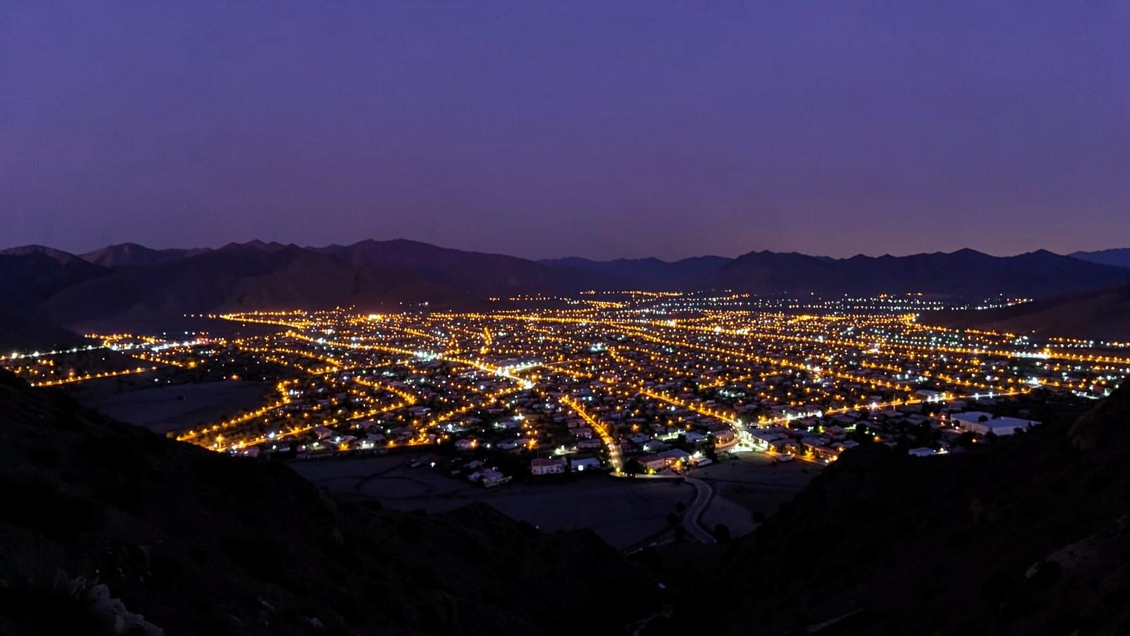 Wide desert valley city spreading across a flat basin at dusk with amber street lights and silhouetted mountains
