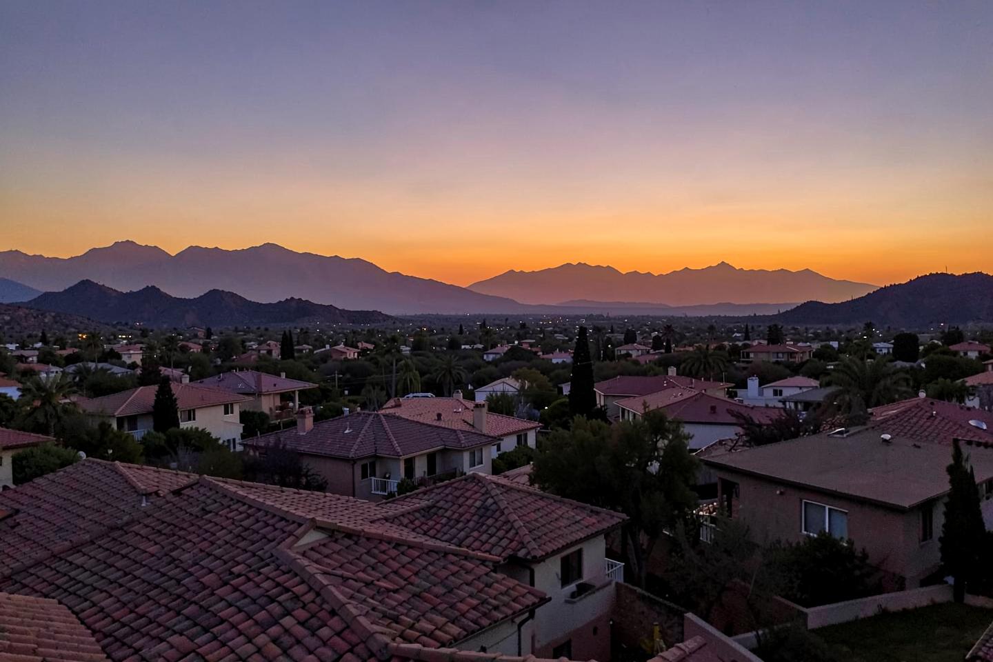 Wide dusk view over a desert suburban valley of tile rooftops with mountain silhouettes and warm sky
