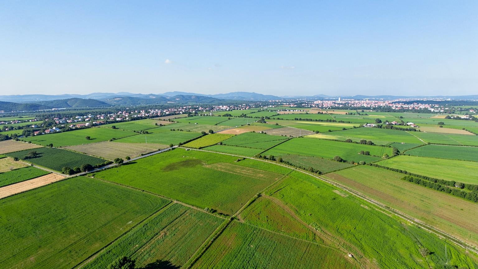 Wide aerial view over a flat patchwork of irrigated crop fields with a small city and low mountains on the horizon