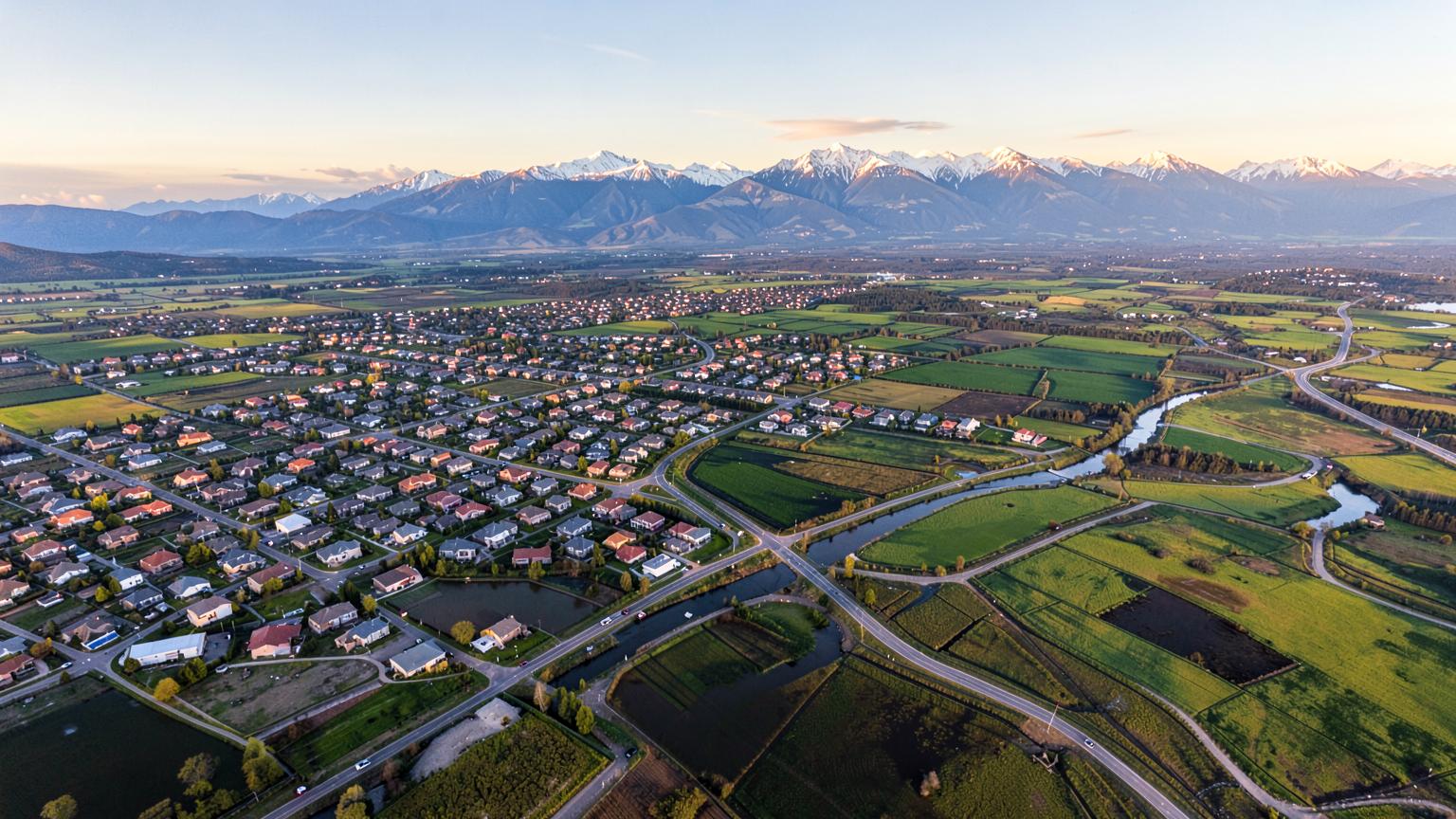 Aerial view of a growing valley where new subdivisions meet irrigated farm fields with snow capped mountains beyond