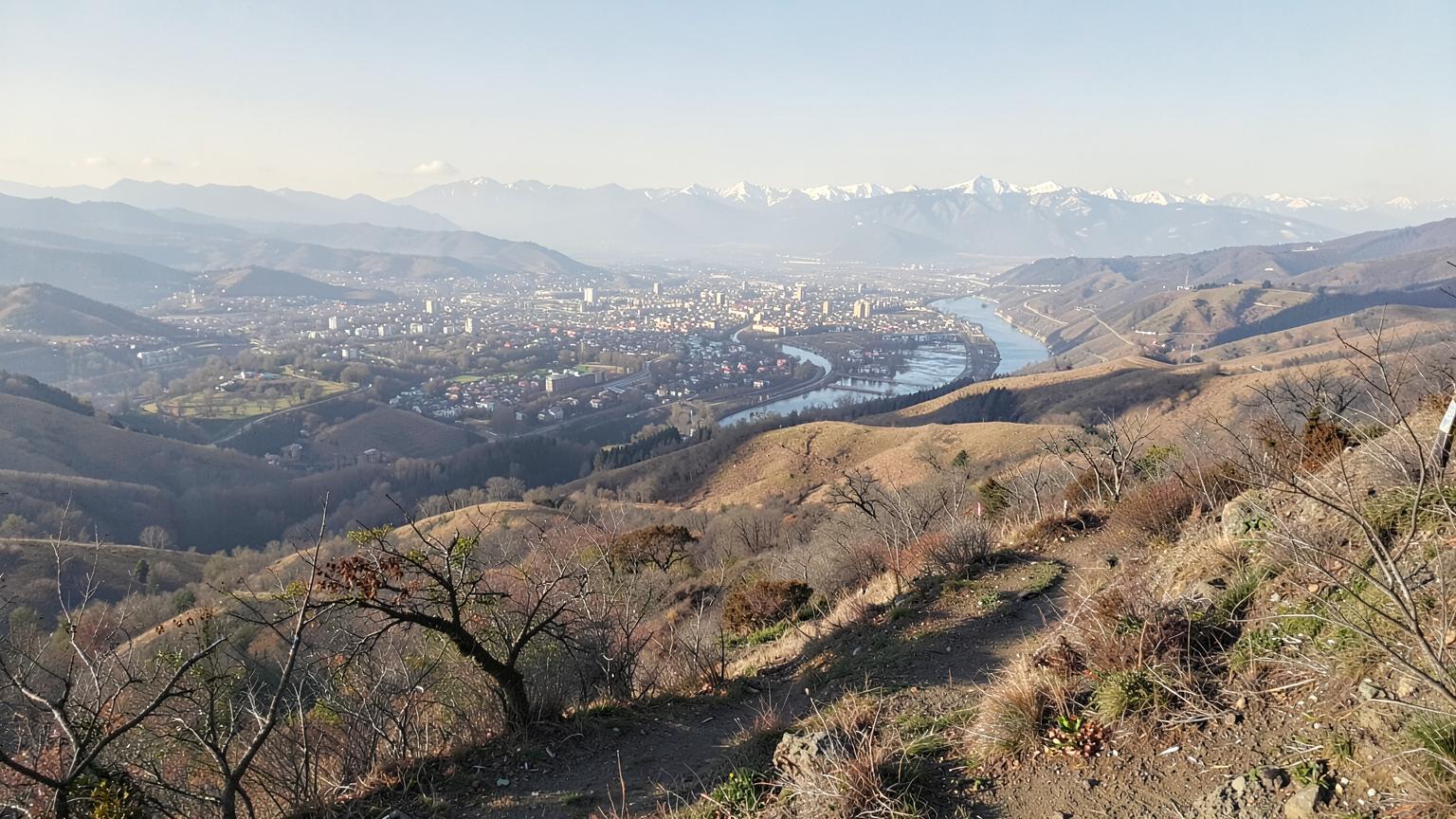 Wide view over a valley of neighborhoods and farmland with a river corridor and snow topped mountains beyond