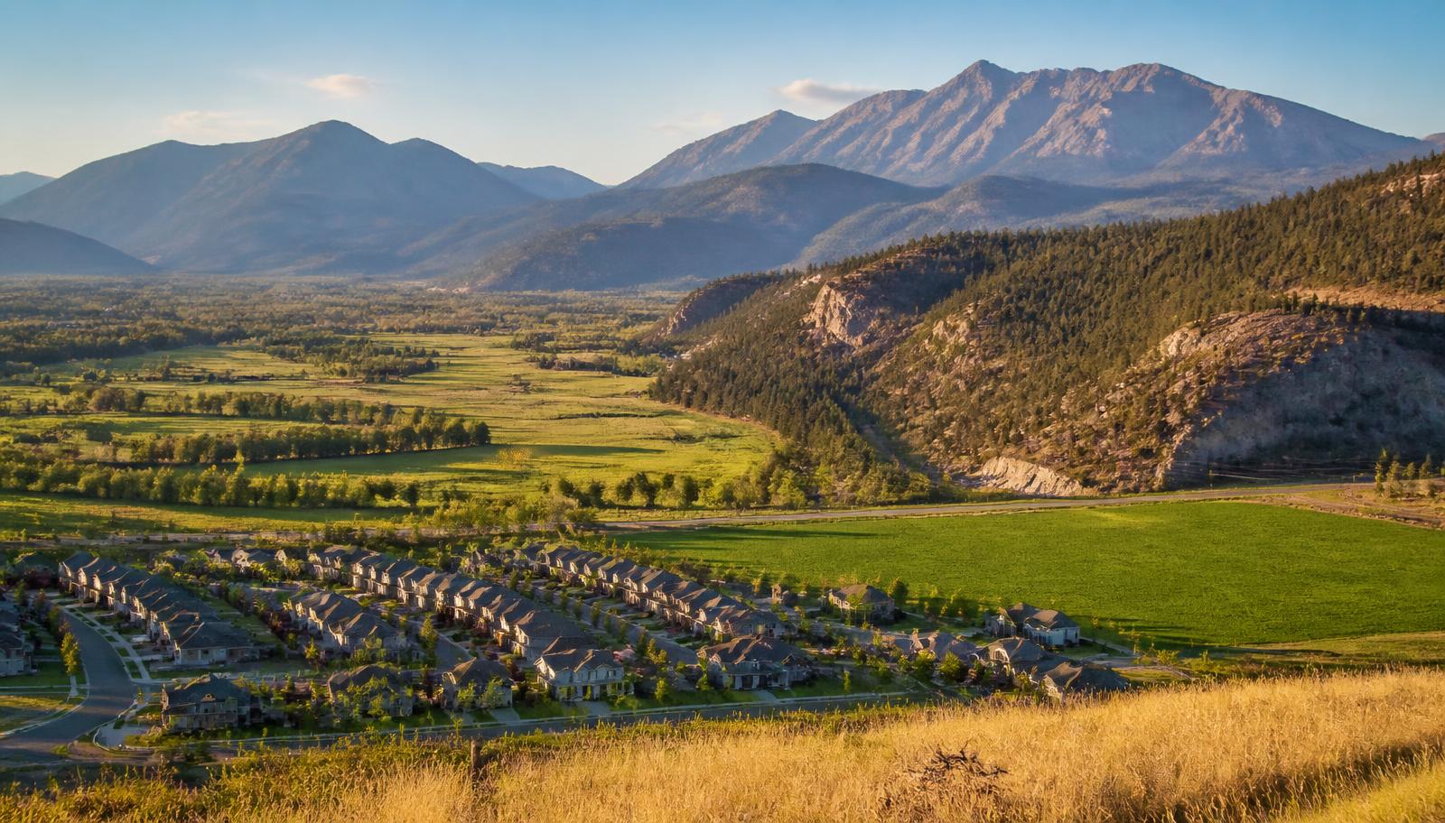 Broad valley panorama where a new subdivision meets green farmland at the mouth of a canyon below tall mountains
