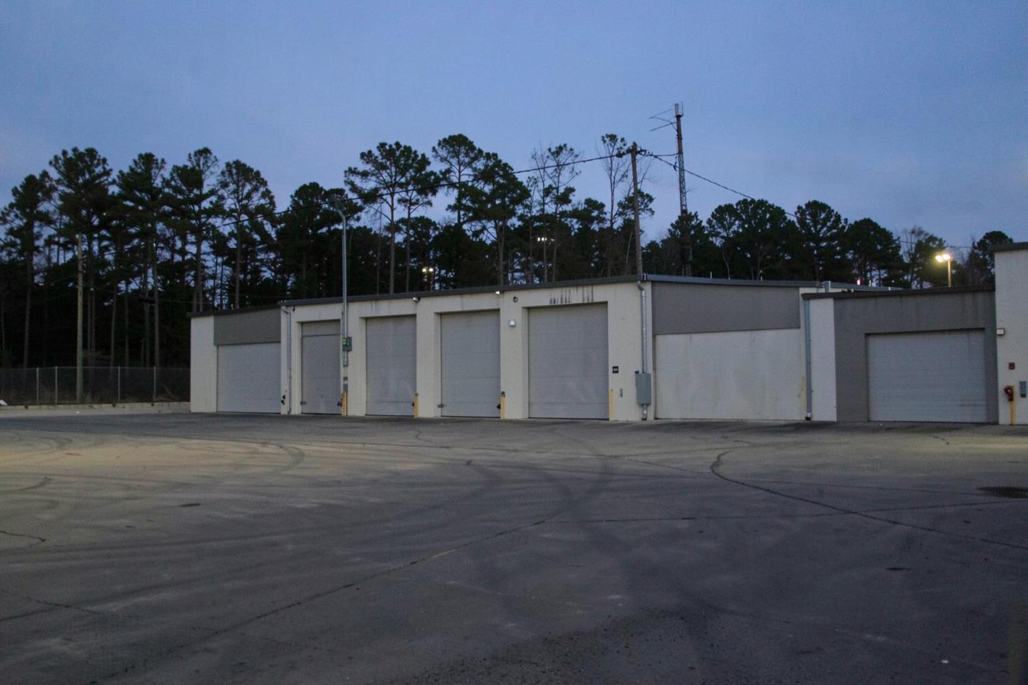Row of plain unmarked loading docks at a large distribution warehouse at dusk with an empty asphalt yard and pine treeline behind