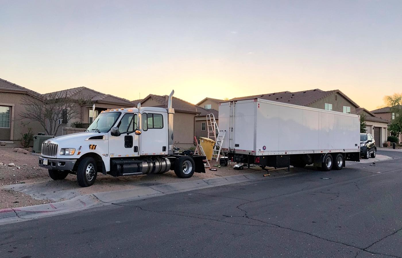 Work truck and utility trailer parked at the curb of a new desert subdivision street at sunrise