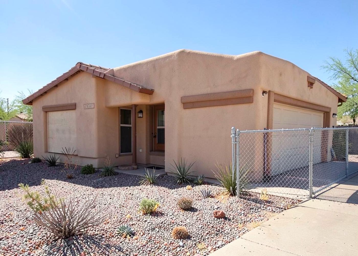 Modest single-story desert home with gravel xeriscape yard, small two-car garage, and chain link side gate