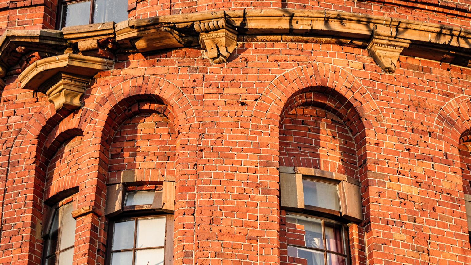 Close view of a historic red brick building facade with tall arched windows and stone sills