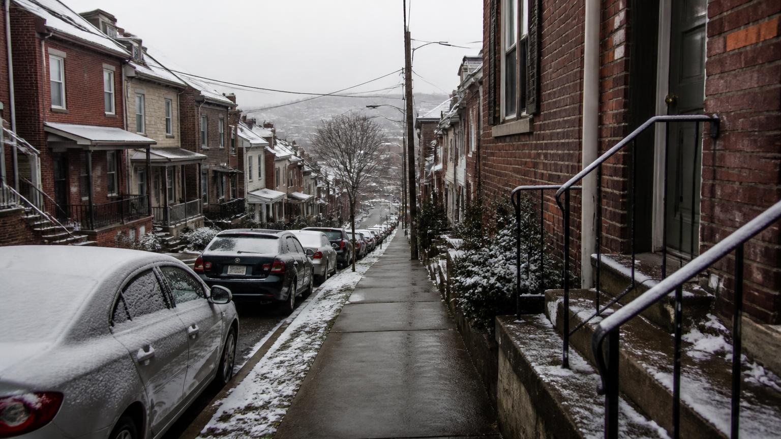 Narrow Pittsburgh hillside street in winter with light snow on brick houses and concrete steps