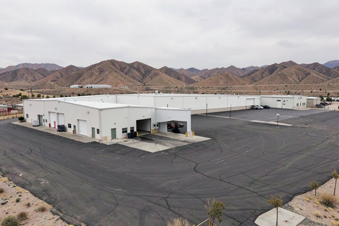 Plain distribution warehouse buildings with loading docks and a wide asphalt yard below dry desert hills