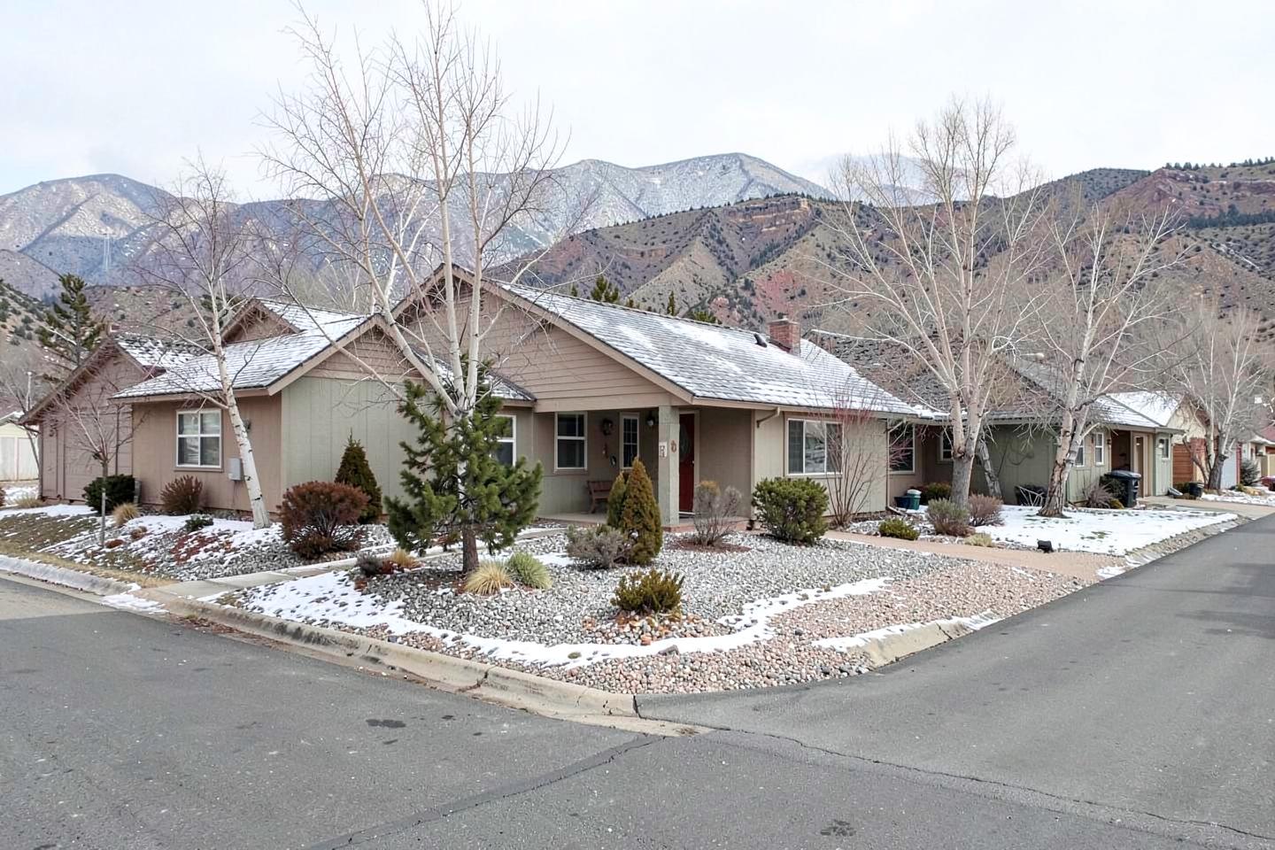 Single-story homes with gravel front yards under light snow on a quiet street below high-desert hills